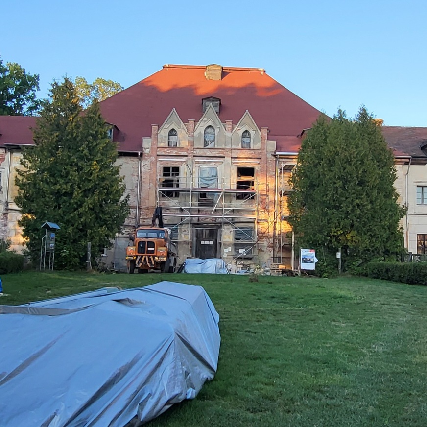 Pałac Lehndorffów w Sztynorcie podczas renowacji, z rusztowaniami i otaczającą zielenią – atrakcja na trasie Zamek w Rynie na Mazurach, historyczna budowla otoczona brukowanym placem – atrakcja w regionie Mazurskiej Pętli Rowerowej.